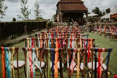 rows of wooden chairs with colorful ribbons on them in front of an outdoor ceremony venue