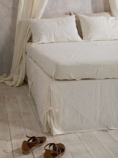 a pair of shoes sitting on the floor next to a bed with white sheets and drapes