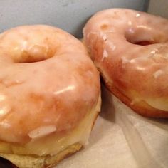 two glazed donuts sitting on top of a piece of wax paper next to each other