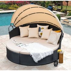 an outdoor day bed with lots of pillows next to a swimming pool in the background