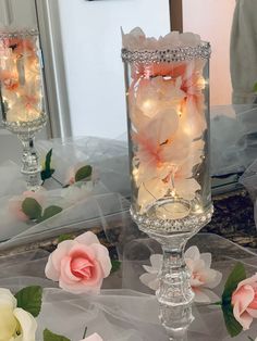 two glass vases filled with flowers on top of a table next to a mirror