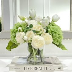 a vase filled with white and green flowers on top of a table next to a mirror