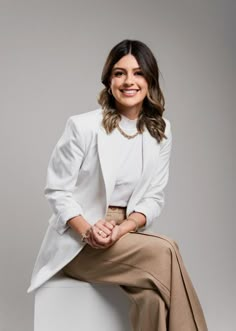 a woman sitting on top of a white stool wearing a skirt and blazer jacket