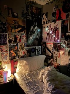 an unmade bed in a bedroom with posters on the wall and lights above it