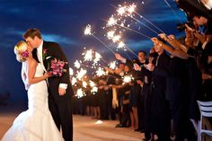 a newly married couple kissing in front of their guests with sparklers coming from them