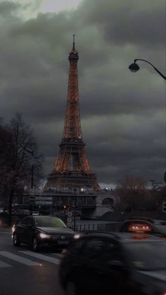 the eiffel tower is lit up at night with cars passing by in front