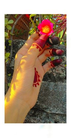 a woman's hand with red and yellow designs on her nails holding a flower