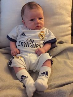 a baby sitting on top of a bed next to a white pillow with the word my emirates written on it