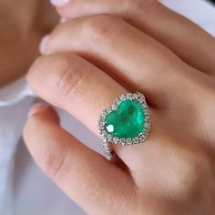 a close up of a person's hand wearing a ring with a heart shaped green stone