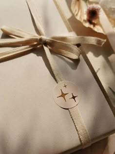 a gift wrapped in white paper and tied with a brown ribbon next to some flowers