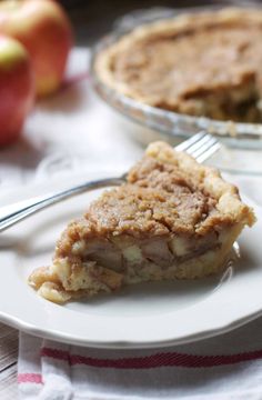 a piece of pie on a plate with a fork next to an apple in the background