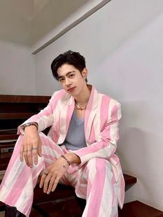 a man sitting on top of a wooden bench wearing a pink and white striped suit