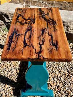 a wooden table sitting on top of a blue metal stand next to rocks and gravel