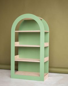 a green book shelf sitting on top of a white floor next to a brown wall