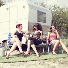 three women sitting on lawn chairs in front of a trailer