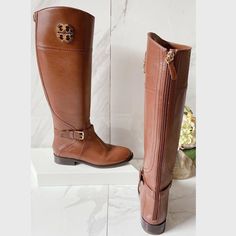 a pair of tall brown boots sitting on top of a white counter next to flowers