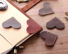 several leather hearts are placed next to an open notebook on a wooden table with a penny