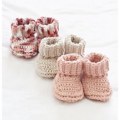 four crocheted baby booties are lined up on a white surface, one is pink and the other is brown