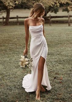 a woman in a white dress holding a bouquet and walking through the grass with her hand on her hip