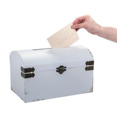 a hand holding a piece of paper over a white trunk with writing on the lid