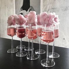 five wine glasses filled with pink and white liquid sitting on a black table next to a mirror