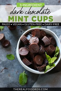 a white bowl filled with chocolate mint cups on top of a gray surface next to mint leaves