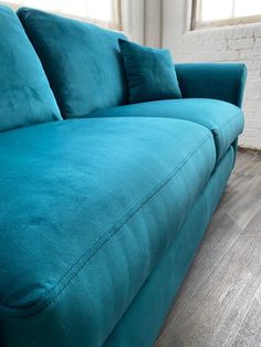 a blue couch sitting on top of a hard wood floor next to a brick wall