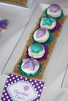 cupcakes in the shape of seashells are displayed on a table with purple and white polka dots