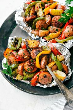 two foil packets filled with sausages and peppers on top of a black platter