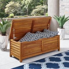 a wooden storage bench sitting on top of a blue rug next to potted plants