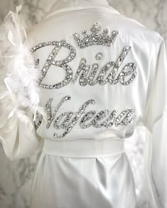 the back of a bride's jacket with white feathers on it and words written in silver