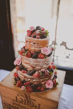 a three tiered cake with strawberries and roses on top is sitting on a wooden box