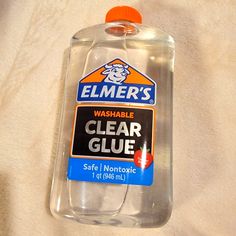 a bottle of clear glue sitting on top of a white bed sheet with an orange cap