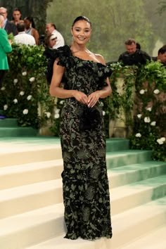 a woman in a black and green dress standing on some steps with people behind her