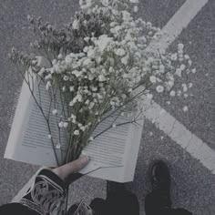 someone is holding a book with flowers in their hand while standing on the street next to them