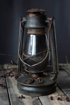 an old metal lantern sitting on top of a wooden table next to dried berries and twigs