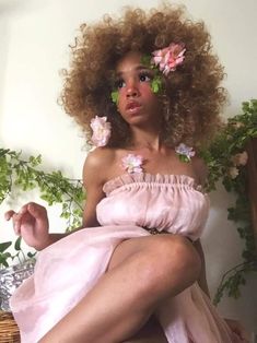 a woman in a pink dress sitting on a chair with flowers around her neck and legs