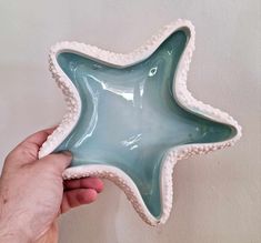 a hand holding a glass starfish dish in front of a white wall