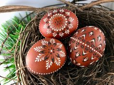 three painted eggs sitting in a nest on the ground