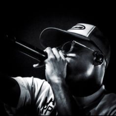 a man wearing glasses and a baseball cap is holding a microphone to his mouth while looking into the distance