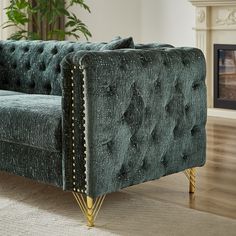 a green velvet couch sitting on top of a wooden floor next to a fire place