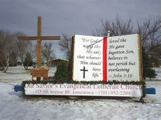 a large wooden cross sitting in the snow next to a sign with words on it