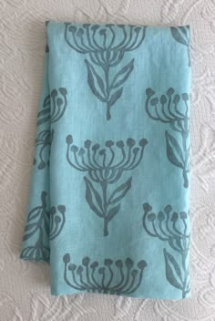 two teal colored napkins sitting on top of a white tablecloth covered in blue flowers