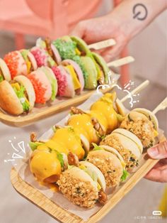 two trays filled with different types of food on wooden sticks and one holding a plate full of sandwiches