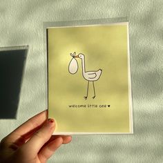 a hand holding up a card with a bird on it's back and the words welcome little one