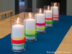 several candles are lined up on a table with blue mat and wooden chairs in the background