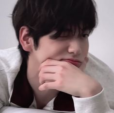 a young man with his chin resting on his hand while wearing a white shirt and tie