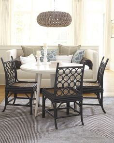 a dining room table with four chairs and a couch in front of the window,