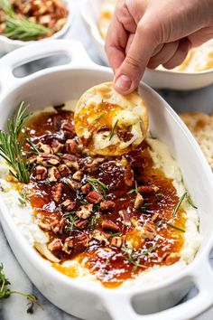 a person dipping some kind of food into a bowl filled with mashed potatoes and pecans