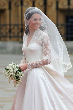 the bride is smiling as she walks down the street in her wedding dress and veil